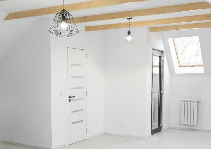 A professionally deep-cleaned, empty room with white walls, exposed wooden beams, and a skylight.