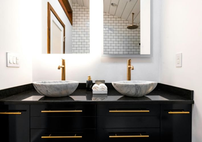 A pristine, professionally cleaned modern bathroom with a black vanity, gold faucets, and two marble vessel sinks.