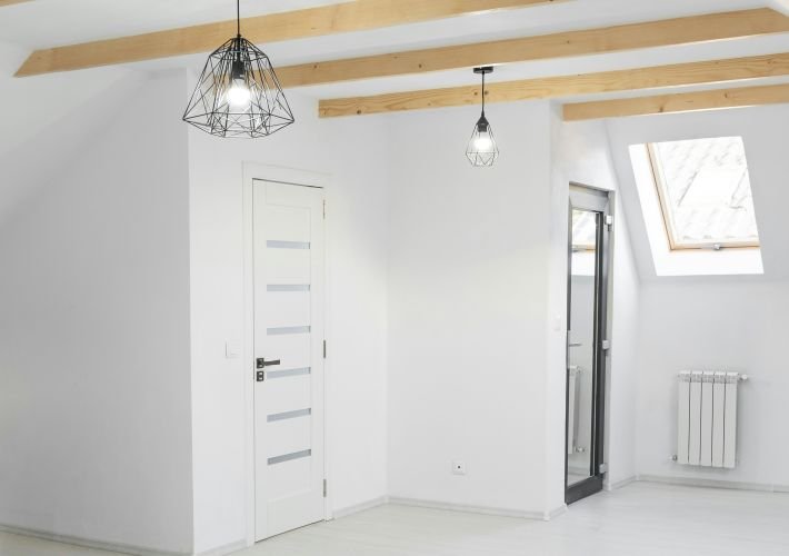 A professionally deep-cleaned, empty room with white walls, exposed wooden beams, and a skylight.